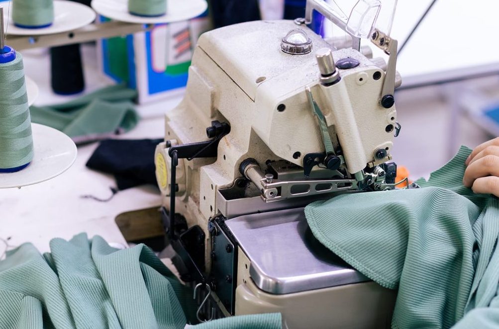 Personne qui coud un tissu vert dans une usine de fabrication textile